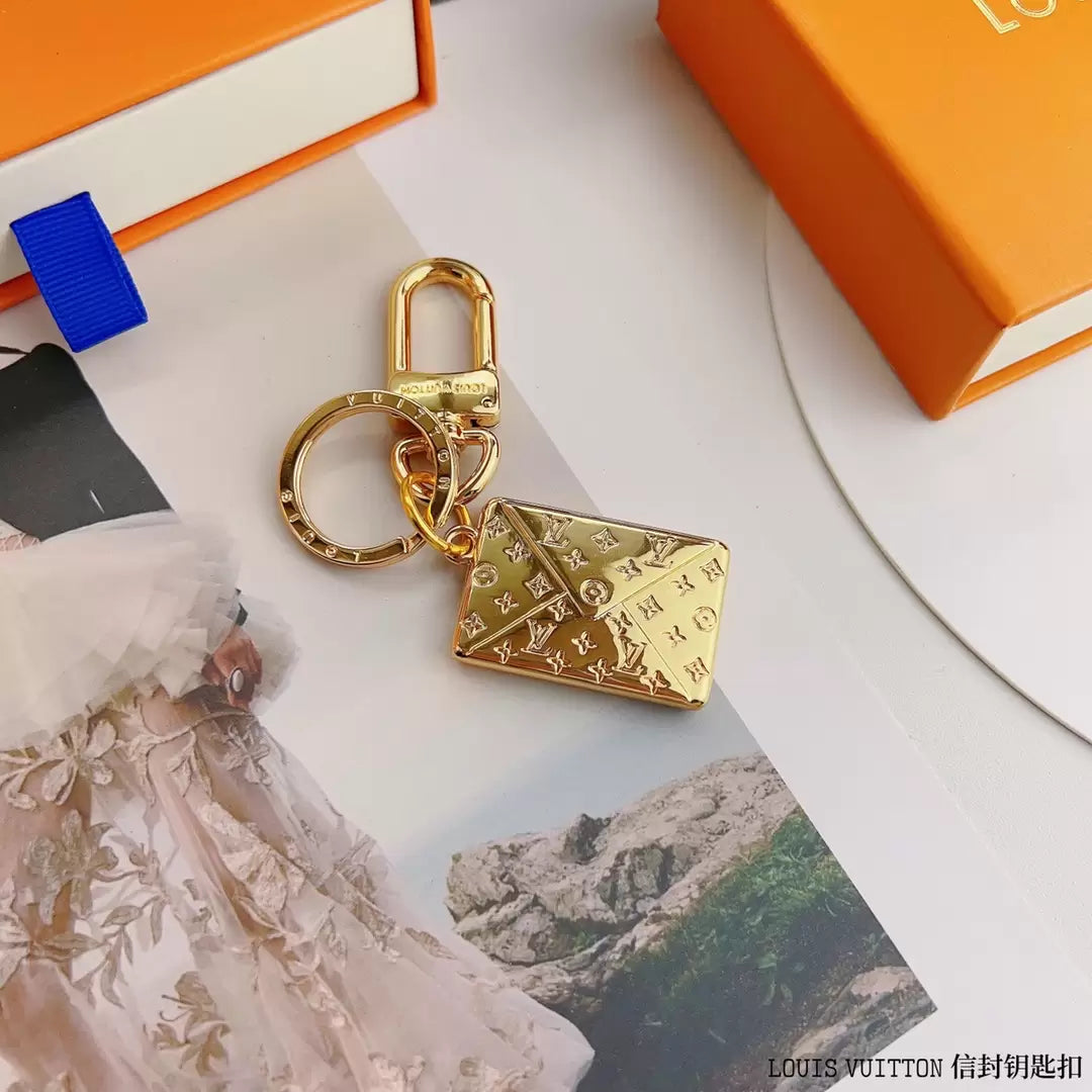 Envelope-shaped gold-tone keychain shown beside orange packaging