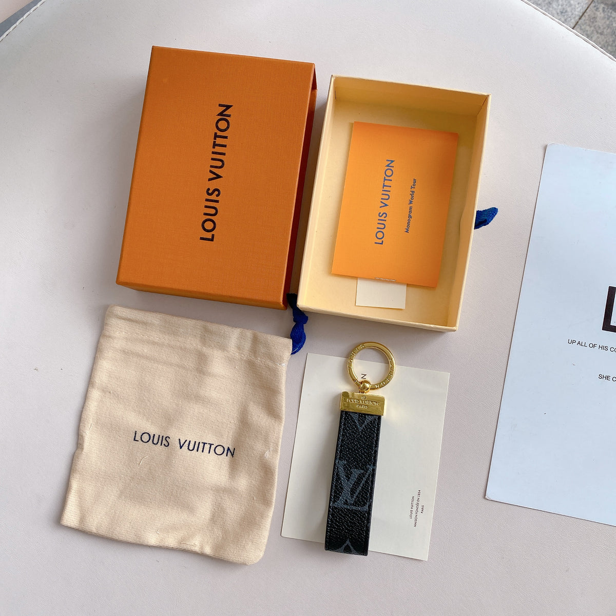 Black oversized monogram key holder shown beside orange packaging
