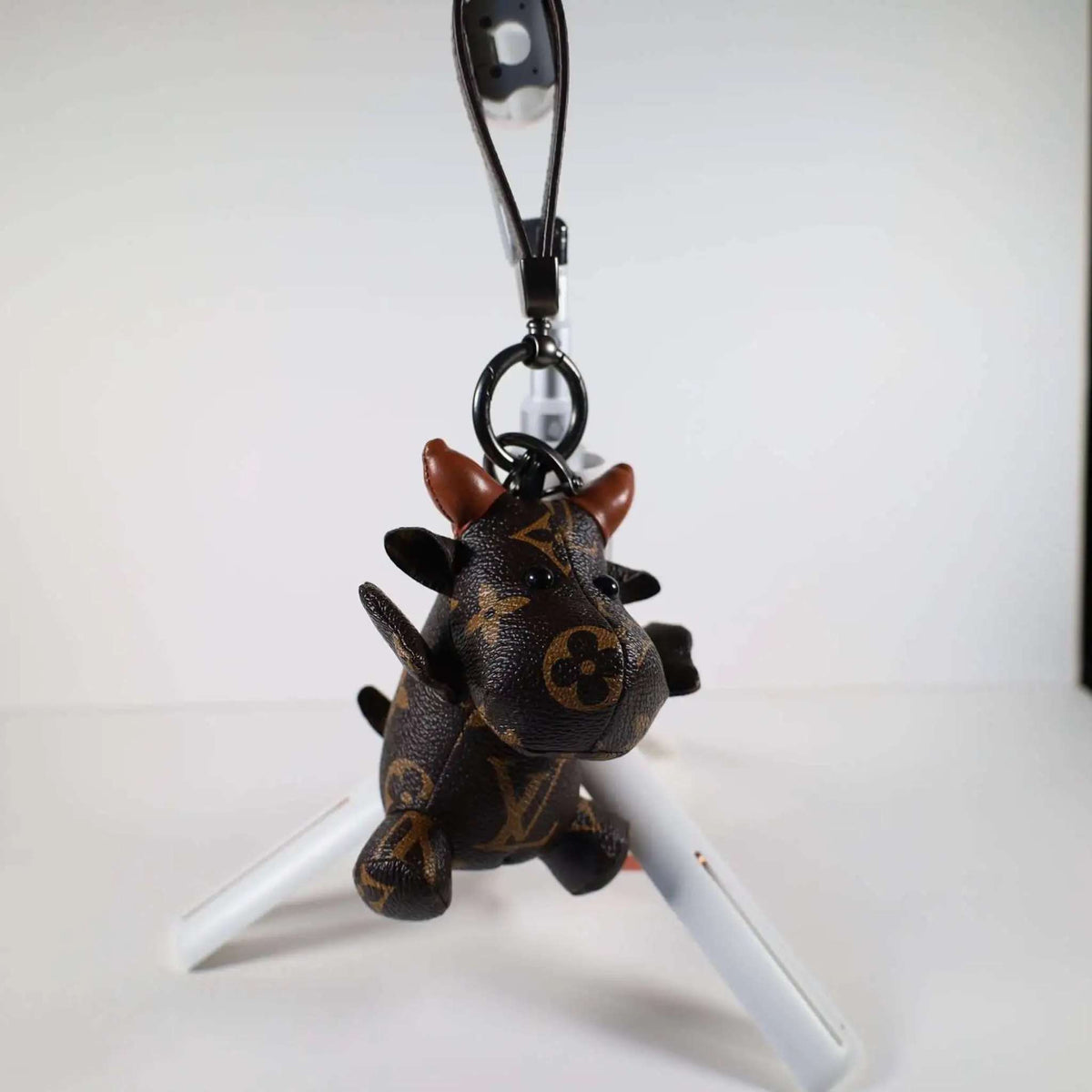 Cow keychain hanging from its wrist strap above a white stand