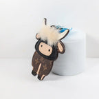 Side view of flat cow charm leaning against a white cylinder