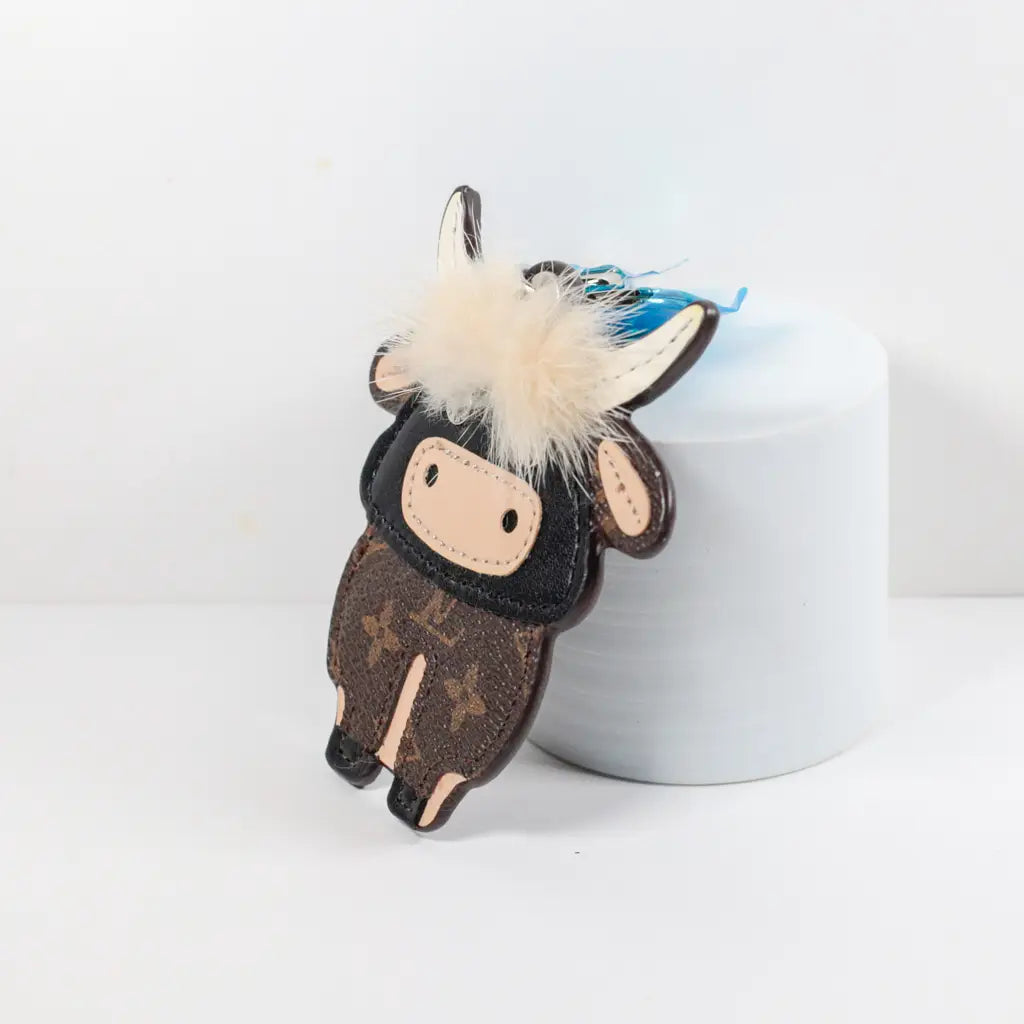 Side view of flat cow charm leaning against a white cylinder