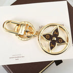 Circular gold-tone keychain with dark monogram flower center