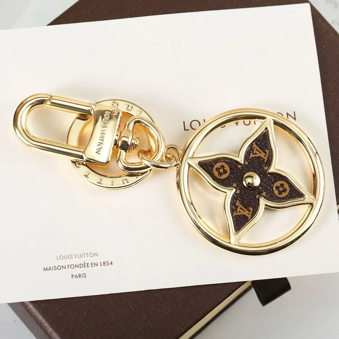 Circular gold-tone keychain with dark monogram flower center