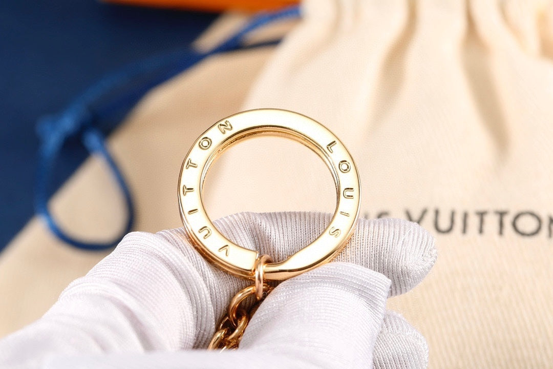 Engraved gold-tone keyring held above a fabric pouch