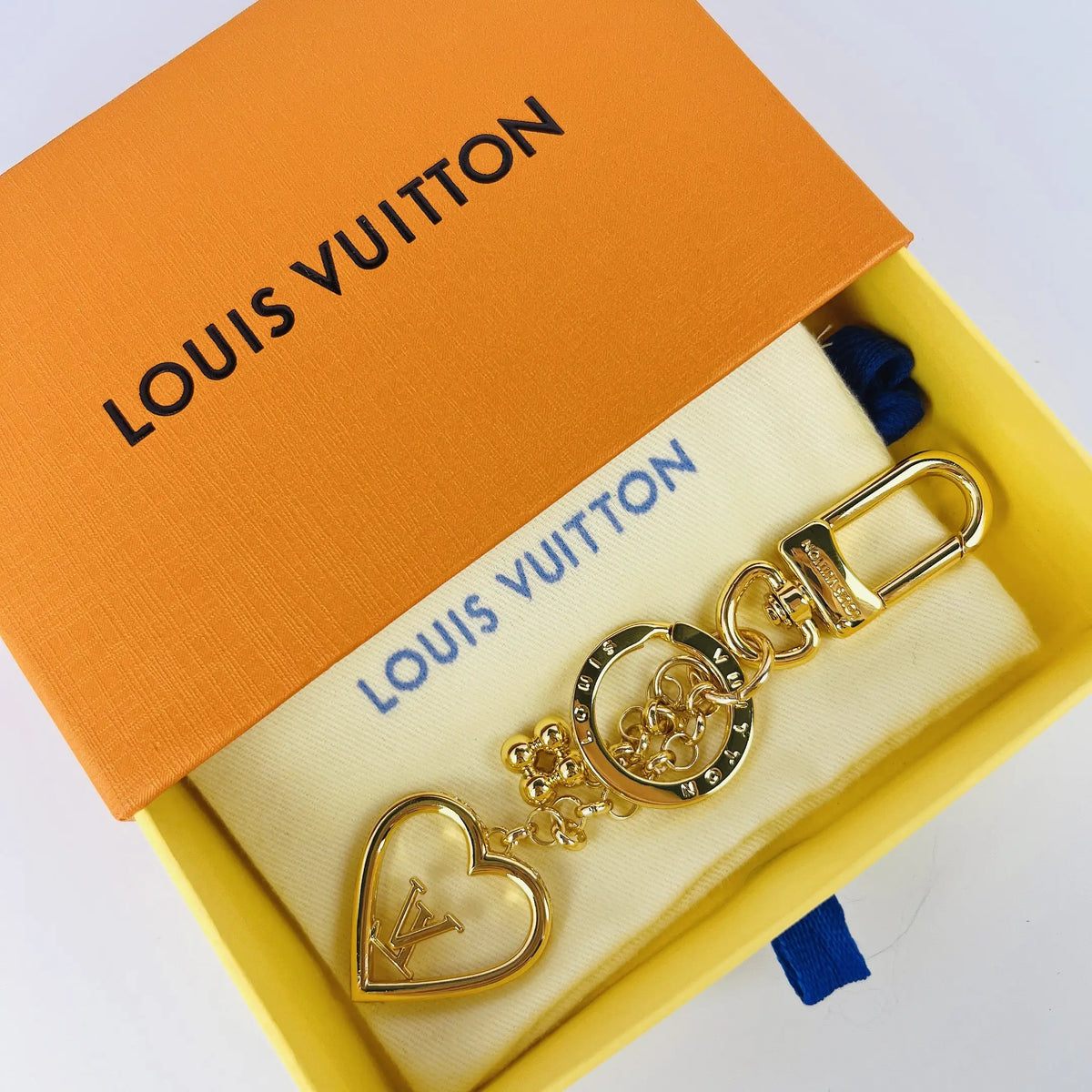Gold-tone heart keychain arranged on a pouch inside a box