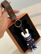 Bunny keychain lifted by its monogram strap above an open box