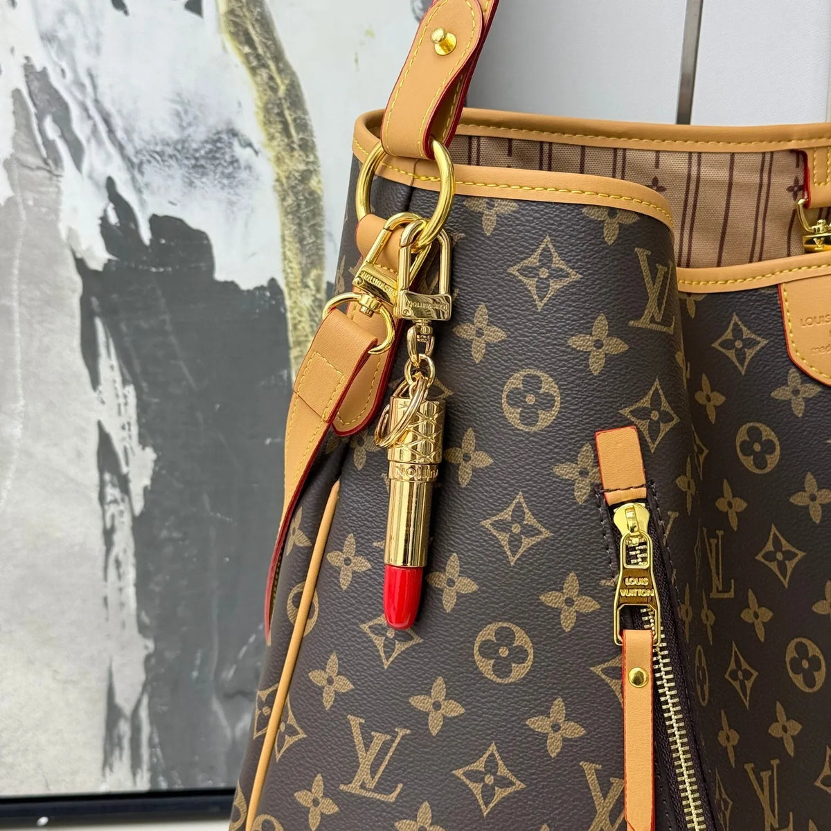 Gold-tone lipstick charm attached to a brown monogram bag