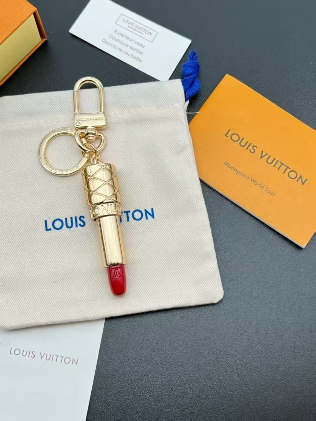 Gold-tone lipstick keychain with red tip on a fabric pouch