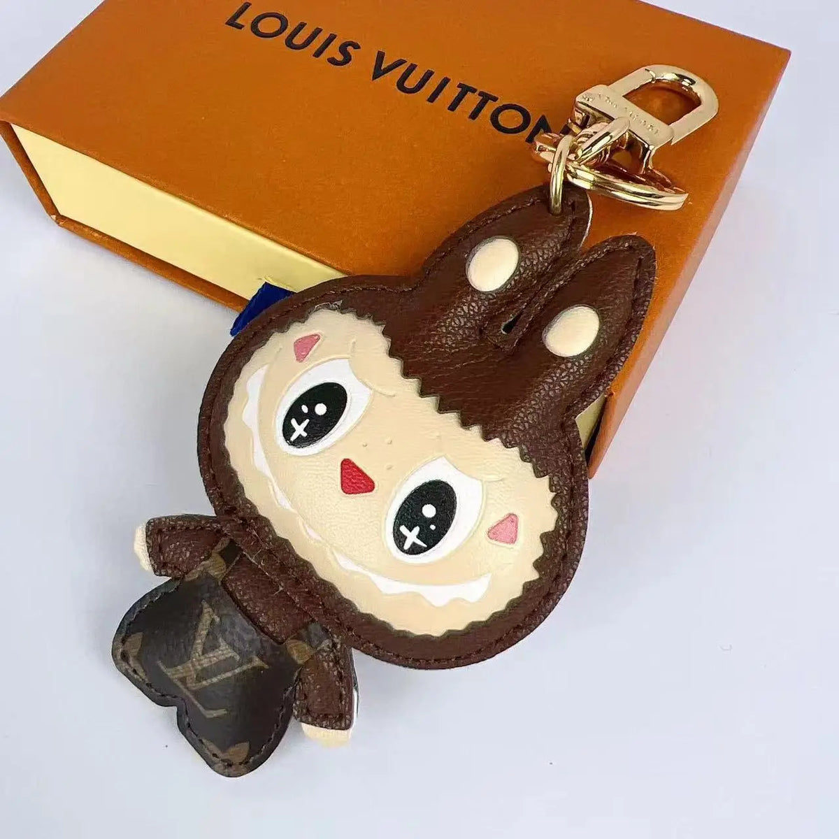 Brown Labubu keychain with gold-tone clasp beside an orange box