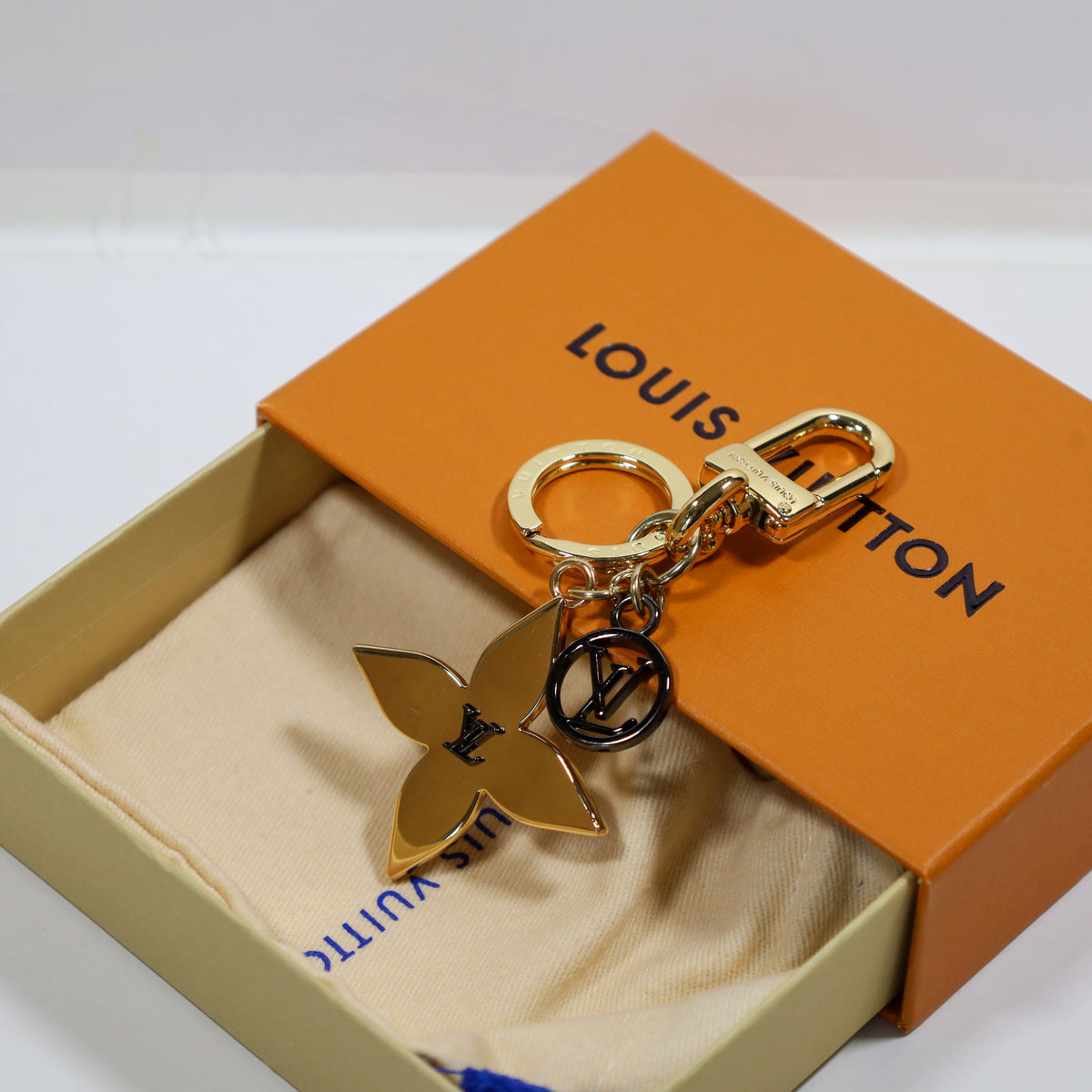 Gold-tone flower pendant and round LV charm beside packaging