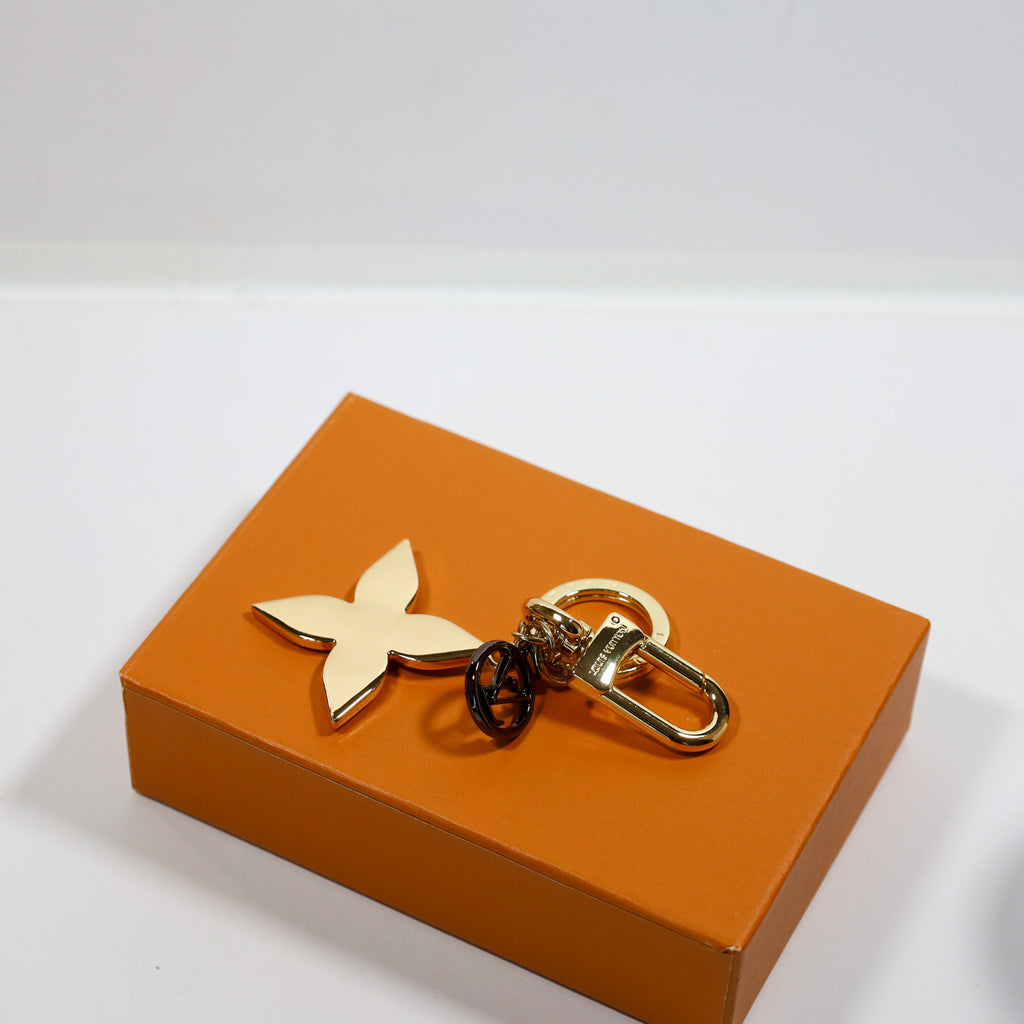 Gold-tone floral keychain laid flat showing dark round pendant