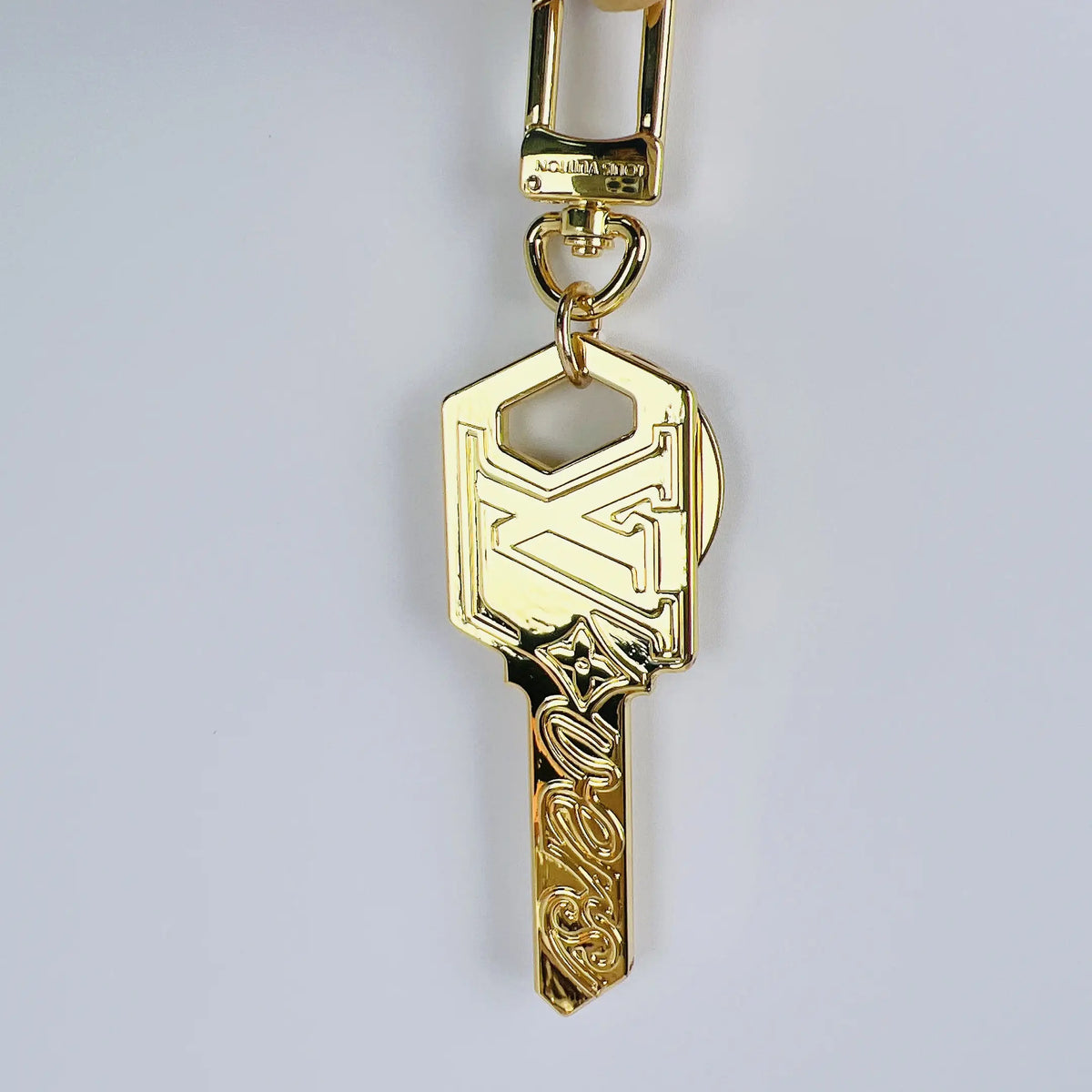 Gold-tone LV key pendant hanging vertically from its clasp
