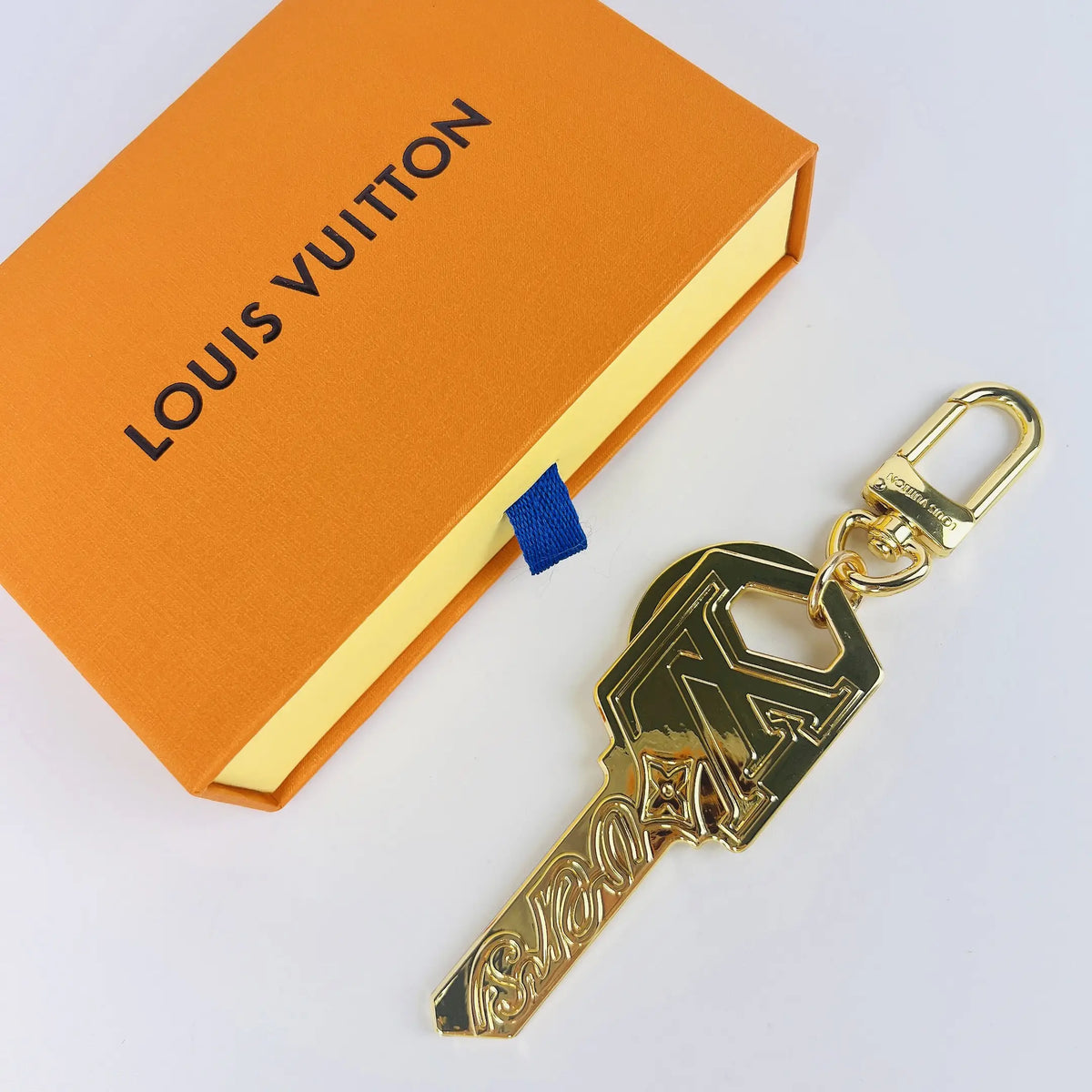 Gold-tone LV key-shaped keychain beside an orange box