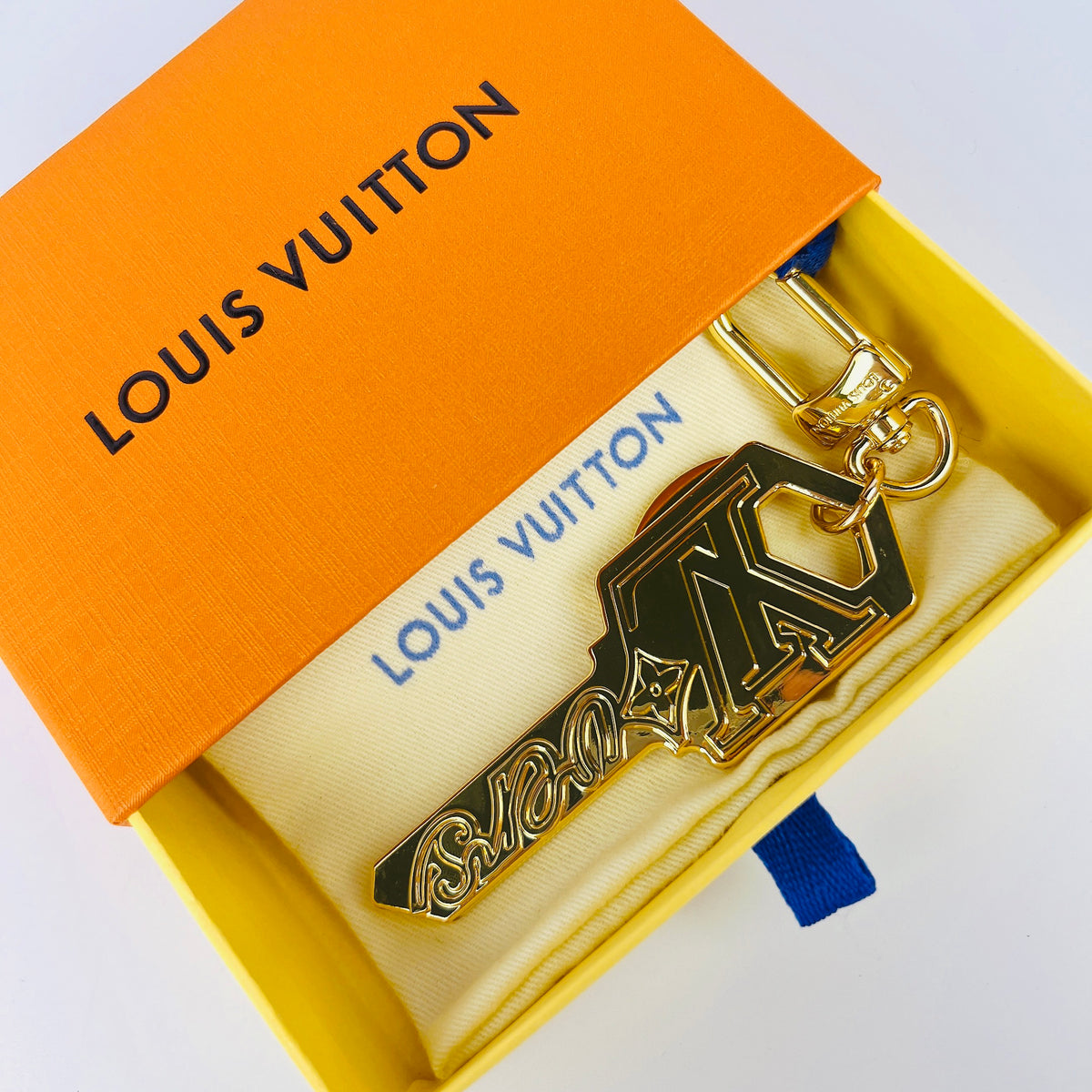 Gold-tone key-shaped LV charm resting inside an orange box