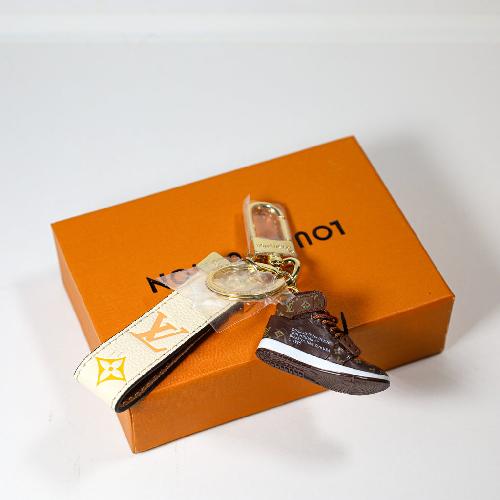 Brown sneaker pendant beside gold-tone clasp and cream strap