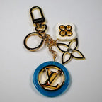 Gold-tone keychain with blue circular LV pendant and floral charms
