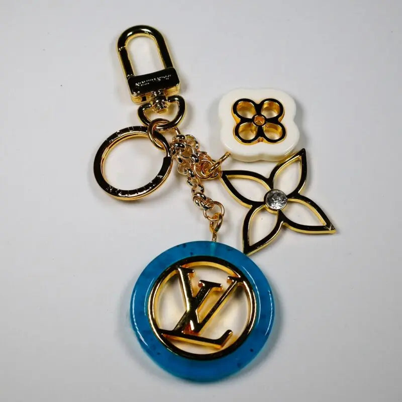 Gold-tone keychain with blue circular LV pendant and floral charms