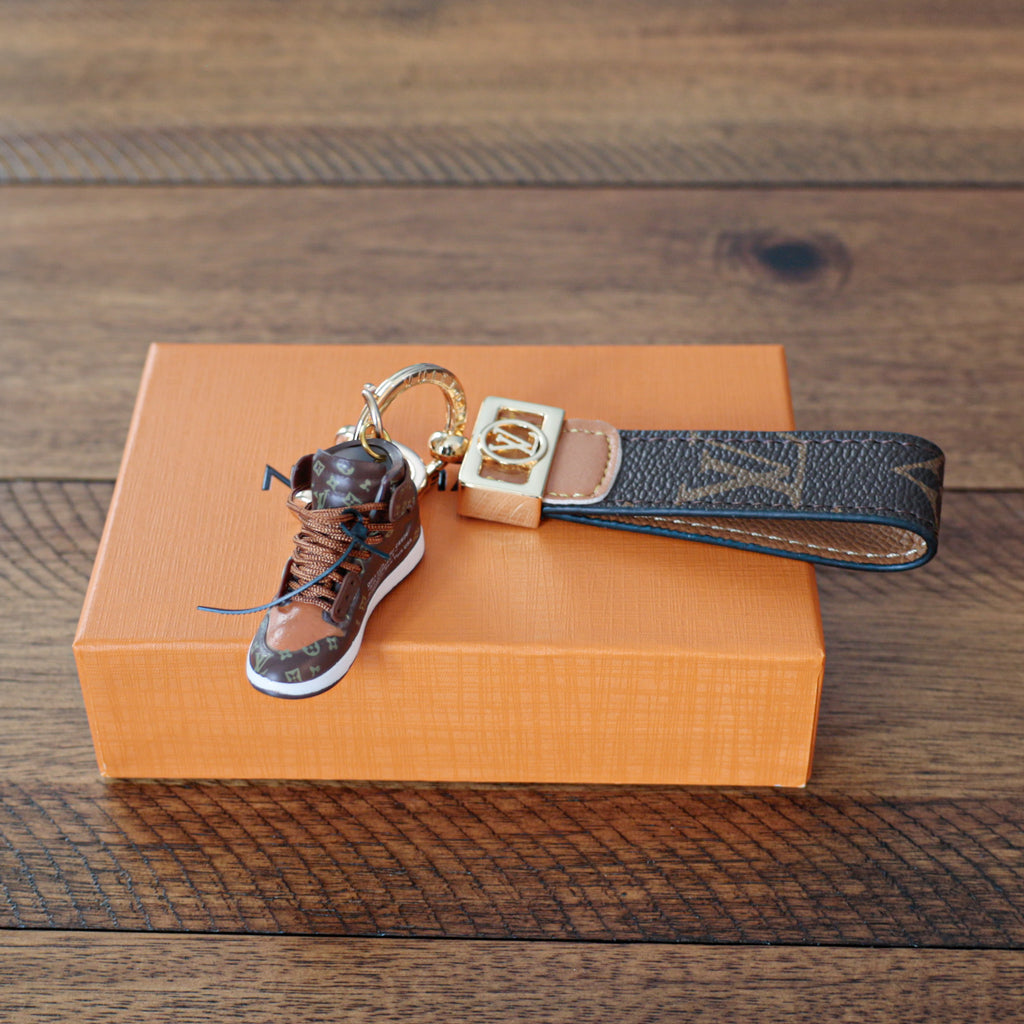 Brown sneaker keychain with dark monogram strap and gold-tone hardware