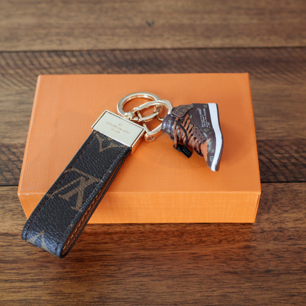 Reverse of dark monogram strap beside brown sneaker charm