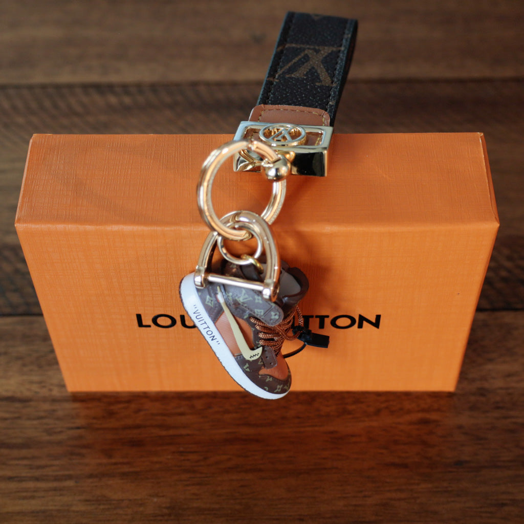 Sneaker charm hanging below dark monogram strap on an orange box