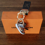 Sneaker charm hanging below dark monogram strap on an orange box